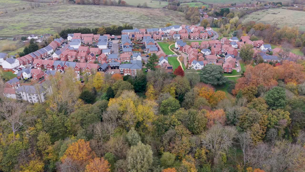 Drone flies over Gilston village, Harlow, Essex. The new estate’s red and grey rooftops, bright grass, yellow paths contrast with surrounding autumn fields and trees, highlighting rural development