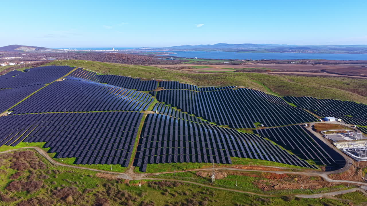 Solpaneler dækker et stort område nær en sø under en klar himmel om dagen, hvilket fremviser vedvarende energiteknologi i naturlige omgivelser.