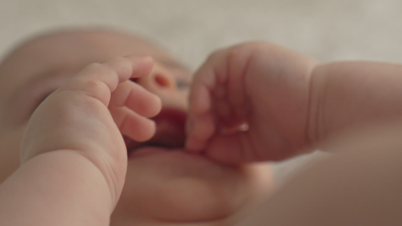 Closeup happy baby boy face, hands, soft light in white bed