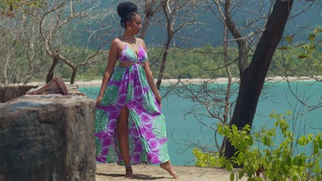 In-Einem-Langen,-Fließenden-Kleid-Gekleidet,-Blickt-Eine-Junge-Frau-Von-Einer-Klippe-Auf-Den-Strand