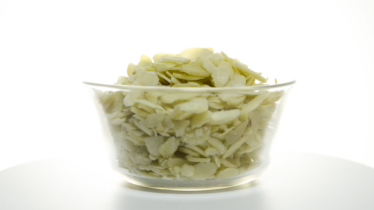 흰색 배경에 얇게 썬 아몬드와 함께 회전하는 투명한 그릇