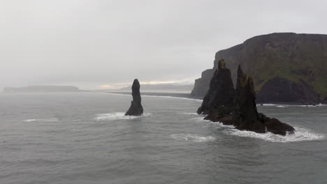 aerial: passing though reynisdrangar sea stacks near reynishjara black sand beach in iceland during harsh weather