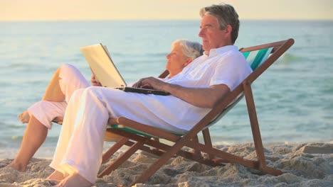 man using a laptop on a beach while his wife sleeps