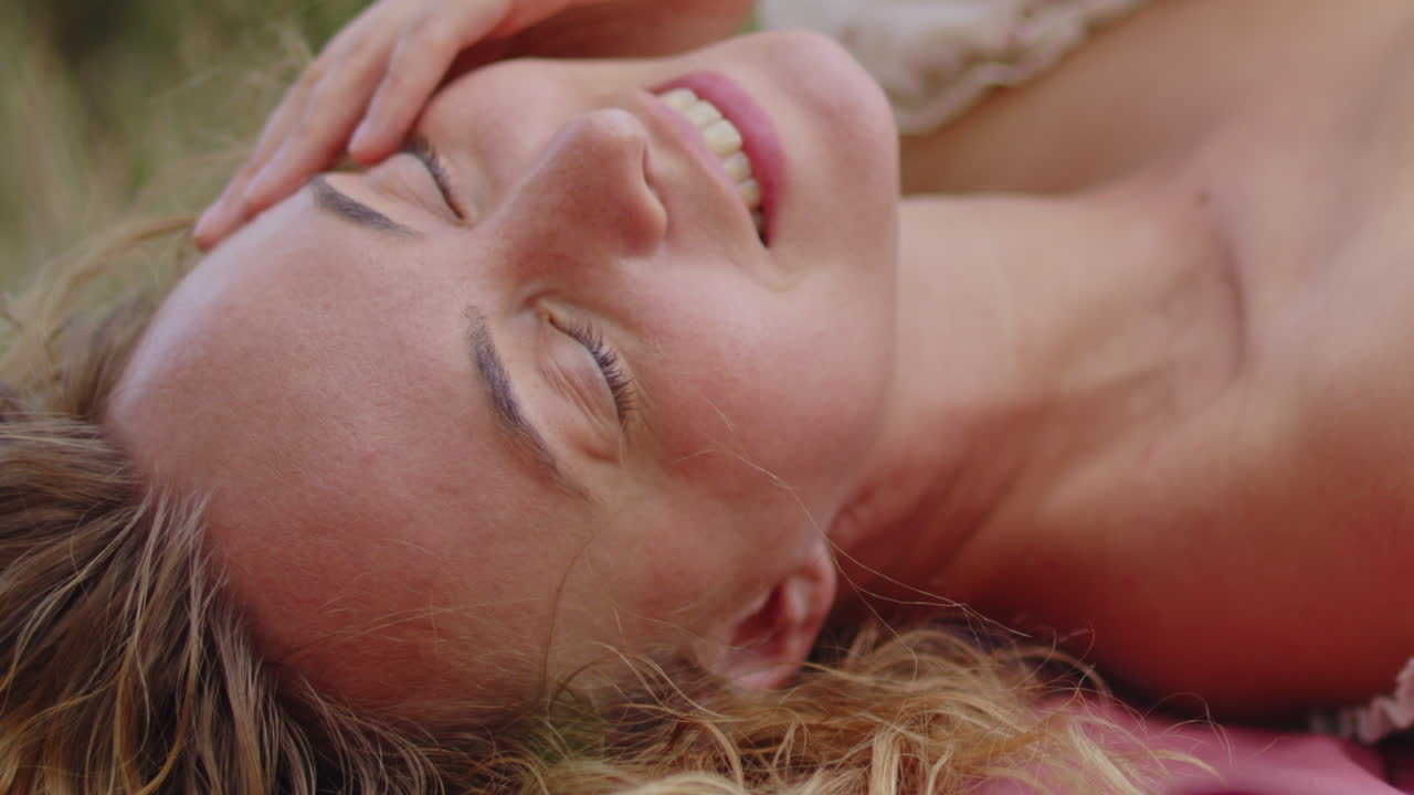 Close up of a beautiful woman biting on her lip while she lies on a green field on a warm summer day