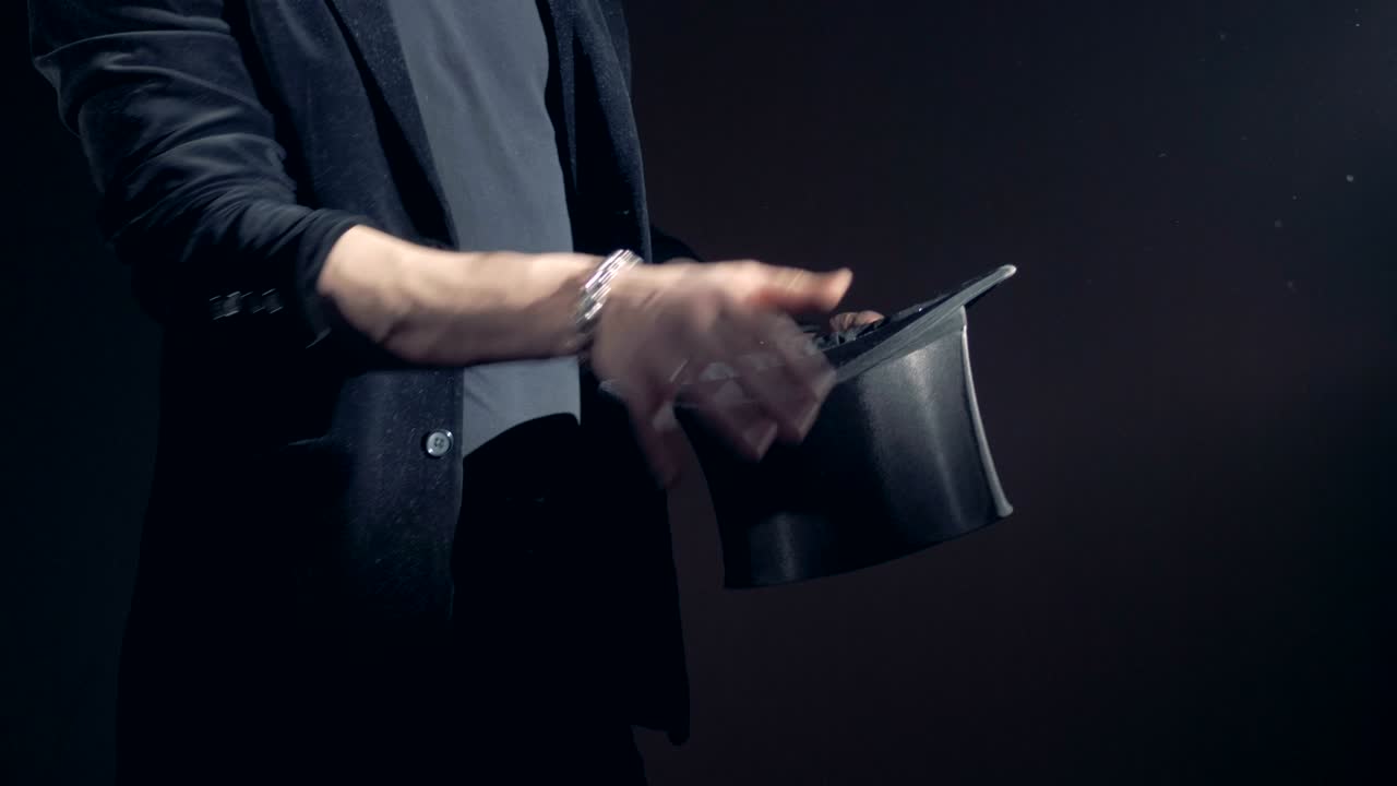 Magician is opening his hat, twisting it and making hand passes.