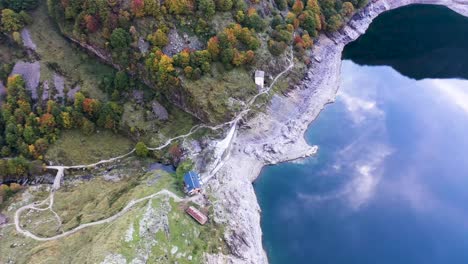 lac d'oô dam stone wall and keeper's cabin at artificial lake in the french pyrenees with water stream, aerial top view orbit around shot