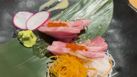 Toro tuna sashimi artfully arranged with wasabi, radish, and garnish on a leaf. Bright lighting enhances the vibrant colors