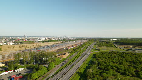 Luftflug-Mit-Fahrenden-Autos-Auf-Der-Autobahn-Neben-Dem-Bahnhof-Und-Der-Stadt-Danzig-Im-Hintergrund,-Polen