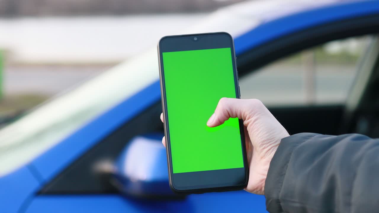 mujer sostiene el teléfono con pantalla verde de maqueta. dispositivo con pantalla verde. llave de croma navegando por internet viendo vídeos de contenido blogs. coche azul en el fondo