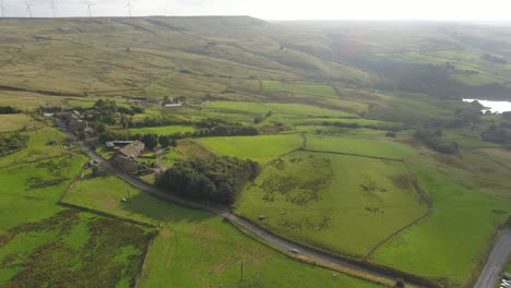 evening drone approach footage of the beautiful rural west yorkshire countryside including farm buildings, fields, moorland, dry stone walls, telegraph poles and wind turbines in the distance