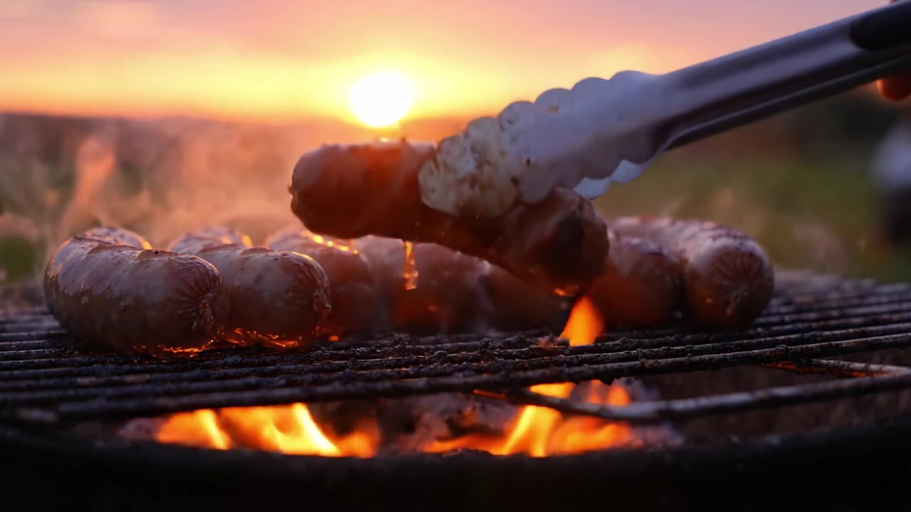 Grigliare salsicce al tramonto: una deliziosa scena di barbecue con fumo, fuoco e il bagliore dorato della luce serale che esalta l'esperienza culinaria.