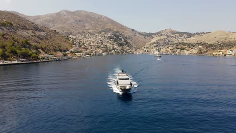 front view of a luxurious mega yacht leaving the bay of symi in greece, drone