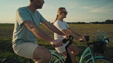 Fröhliches-Kaukasisches-Paar-Mittleren-Alters,-Das-Bei-Sonnenuntergang-Auf-Der-Dorfstraße-Fahrrad-Fährt.