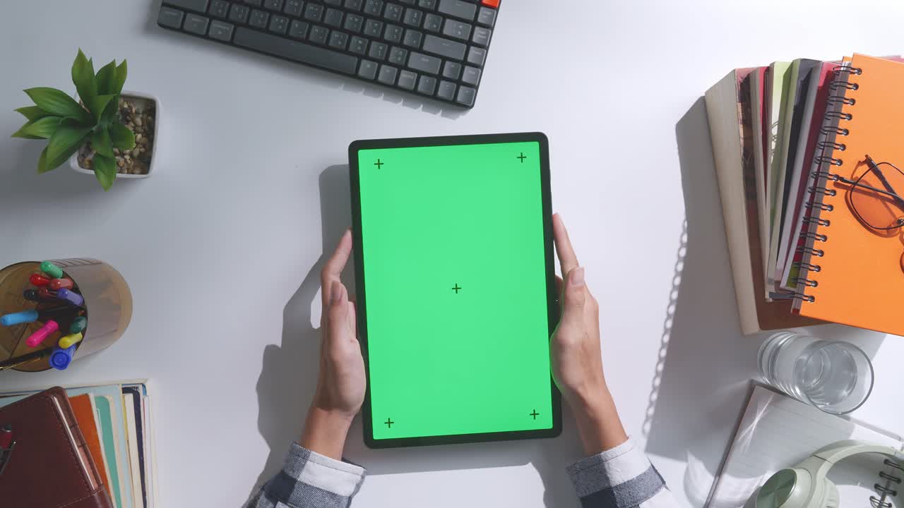 верхний вид ноутбука с макетным зеленым экраном chromakey на деревянном офисном столе рядом с ноутбуком с ручками, очками и стаканом воды.