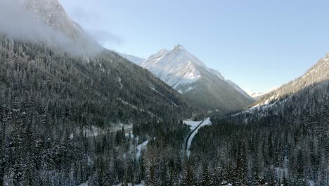 aerial reveal shot of snowy forests and majestic mountains in revelstoke, british columbia: winter wonderland, breathtaking winter landscape from above