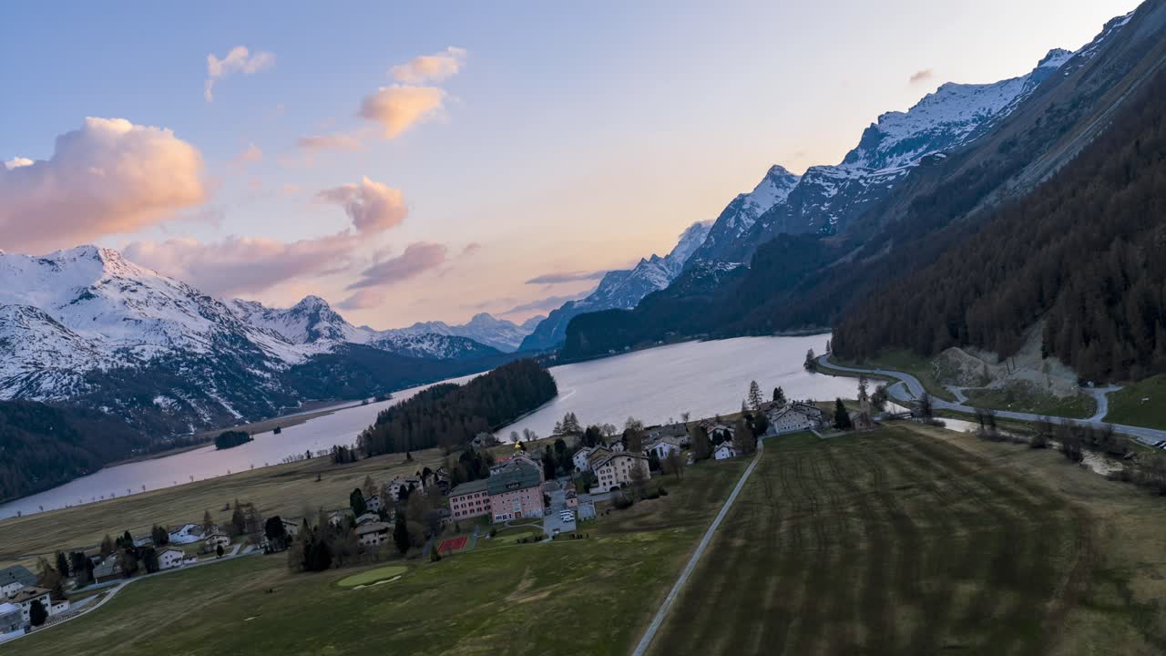 Hyperlapse aereo che mostra il Lago di Silvaplana, il villaggio e le montagne innevate delle Alpi svizzere al tramonto.