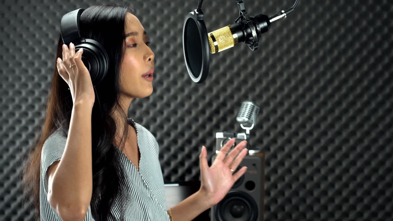 검은색 긴 머리를 감싼 아시아 10대 여성이 마이크 콘덴서와 장비에 매달린 파워 사운드로 큰 소리로 노래를 부른다