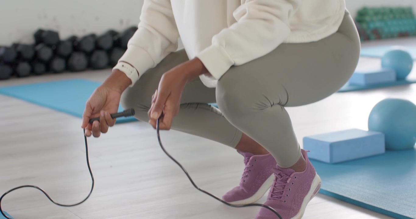African American woman in hoodie jumping rope swing causing stop checking handles to resume in gym