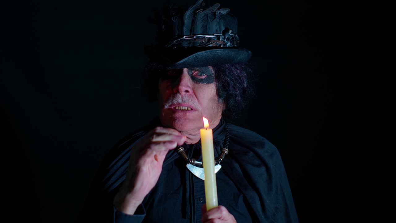 Sinister man with scary Halloween witcher makeup in costume making voodoo magic rituals with candle
