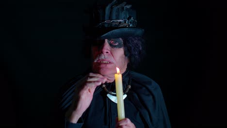 hombre siniestro con miedo halloween brujo maquillaje en disfraz haciendo rituales mágicos vudú con vela