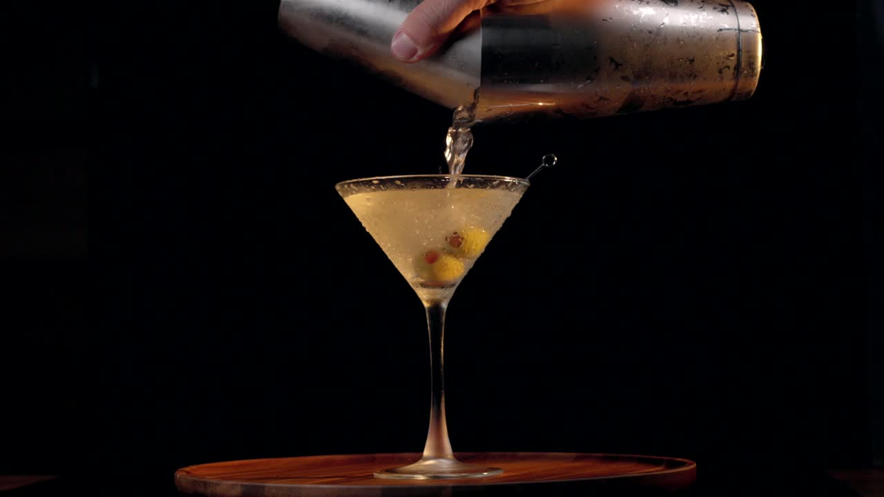 Versare un dirty martini su olive su uno sfondo nero