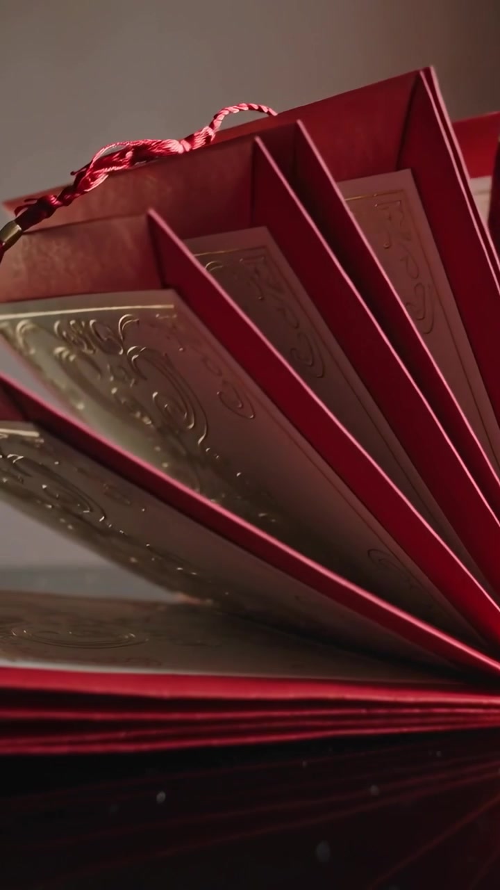 Video verticale: La telecamera fa una panoramica mostrando un folio rosso che si apre a ventaglio su un tavolo con pannelli dorati e una nappa.