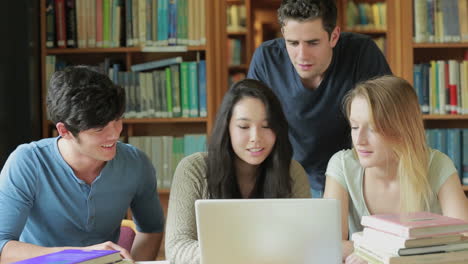 cuatro estudiantes con una computadora portátil en una biblioteca