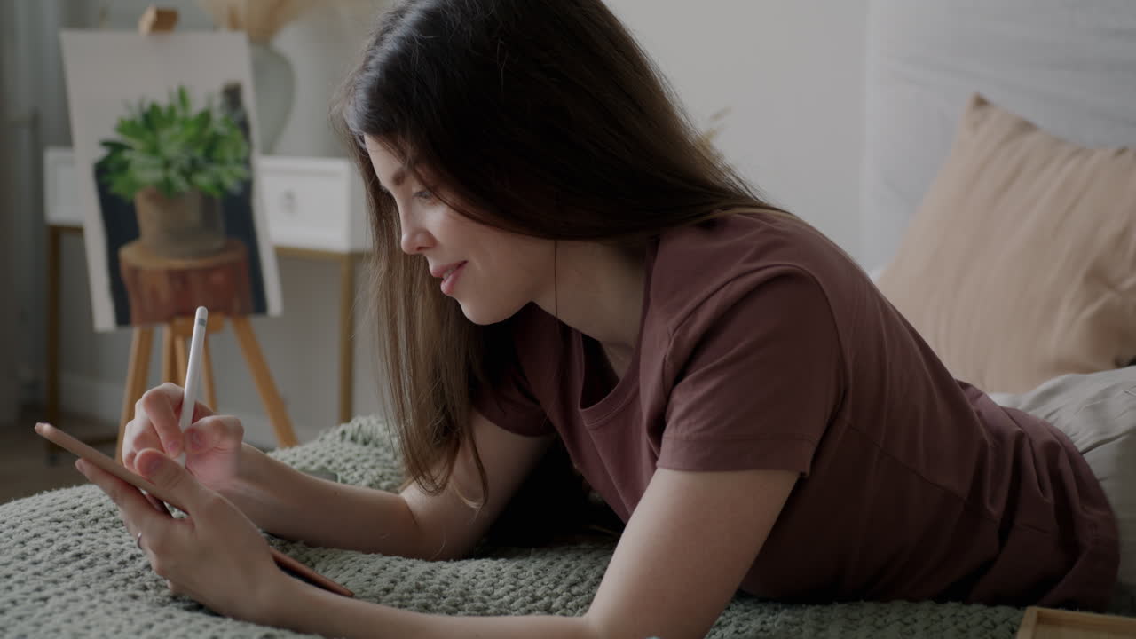 Young woman drawing on a tablet in bed