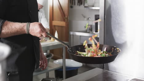 caucasian male chef frying vegetables in a pan in kitchen, slow motion