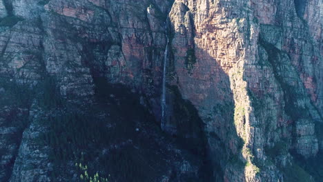 Aéreo---Dron-Ascendente-Con-Cámara-Inclinada-Hacia-Abajo-Revelando-Una-Cascada-Cayendo-Por-El-Imponente-Acantilado-De-La-Montaña-De-Arenisca