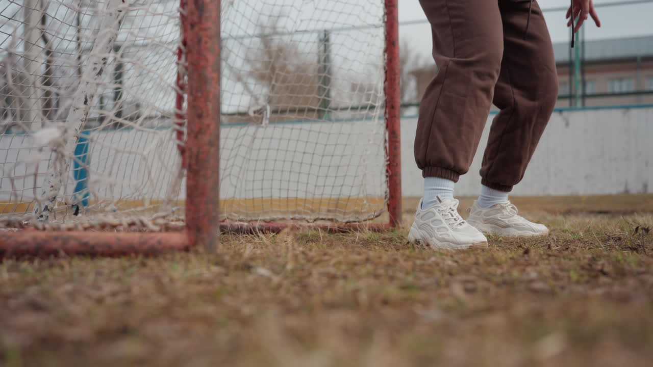 Scena d'azione calcistica, giocatore che calcia rapidamente la palla verso la porta, intenso momento di street soccer con erba e rete materiche, scena dinamica di un giocatore con scarpe bianche che esegue un rapido movimento del piede vicino alla porta