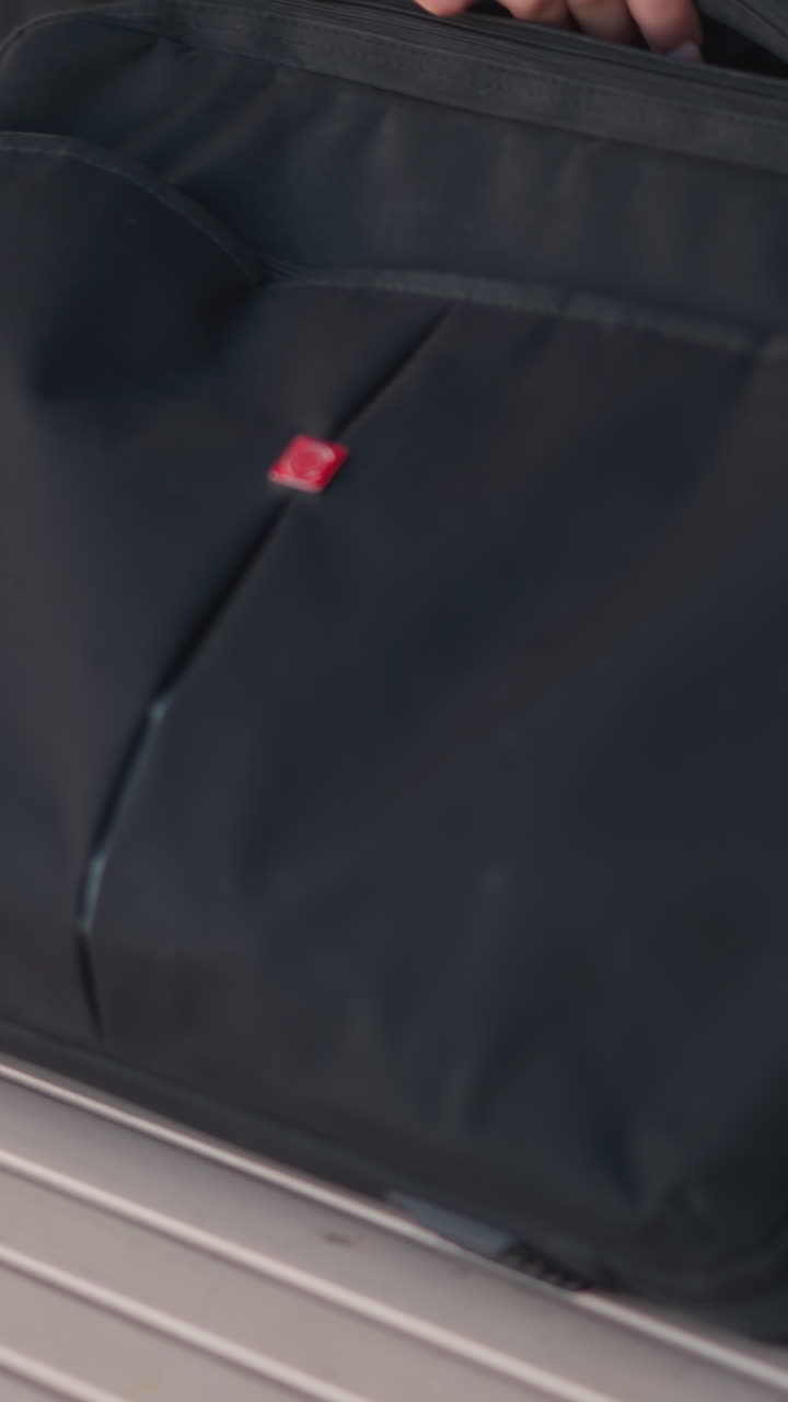 primer plano de una mujer con abrigo negro colocando una bolsa en una mesa de madera, abriéndola con los dedos adornados con anillos, sentada en un entorno al aire libre con flores borrosas y muebles en el fondo