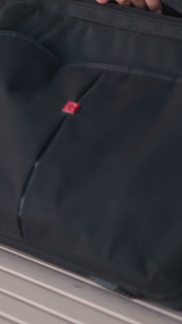 primer plano de una mujer con abrigo negro colocando una bolsa en una mesa de madera, abriéndola con los dedos adornados con anillos, sentada en un entorno al aire libre con flores borrosas y muebles en el fondo