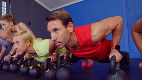 Group-of-people-performing-push-up-with-kettlebell