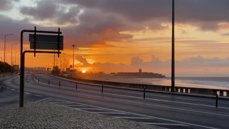 Amplia-Vista-De-Algunos-Autos-Moviéndose-Hacia-Un-Hermoso-Amanecer-Cerca-De-La-Playa-En-Carcavelos,-Portugal