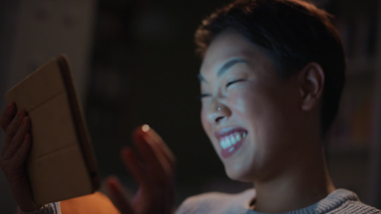 아름다운 아시아 여성이 친구와 늦은 밤에 비디오 채팅을 하고 있습니다.