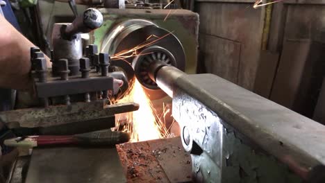 technician is using an electric grinder to grind the work that is being rotated on a lathe.