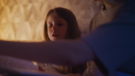 sleepy little child looks through book sitting by mom on bed