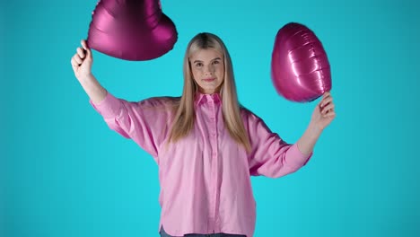 una mujer rubia muy bonita agitando globos de corazón púrpura y luego los lanza, una toma de estudio colorida
