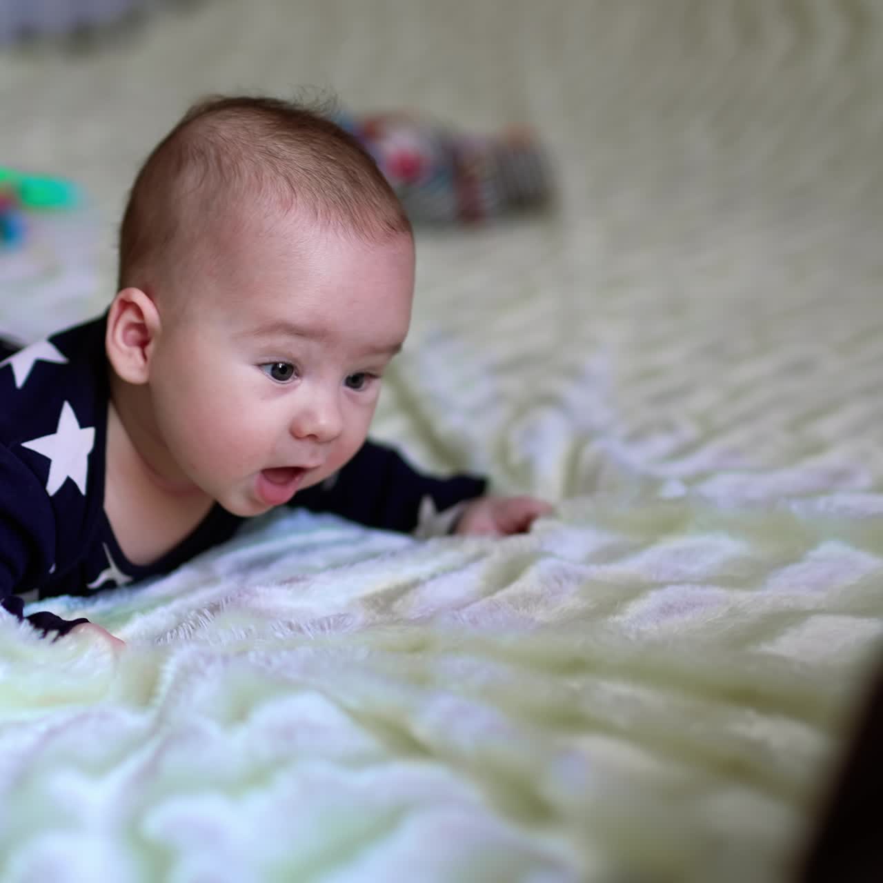 Small adorable baby boy moves actively on bed trying to crawl. Black domestic cat walks by the bed. Blurred backdrop
