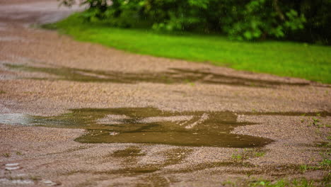 Primer-Plano-Sobre-La-Lluvia-Que-Cae-Sobre-El-Camino-De-Grava-Creando-Charcos-En-El-Paisaje-Rural-En-Un-Día-Lluvioso