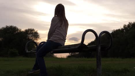 mujer sentada en un banco del parque al atardecer mirando la vista