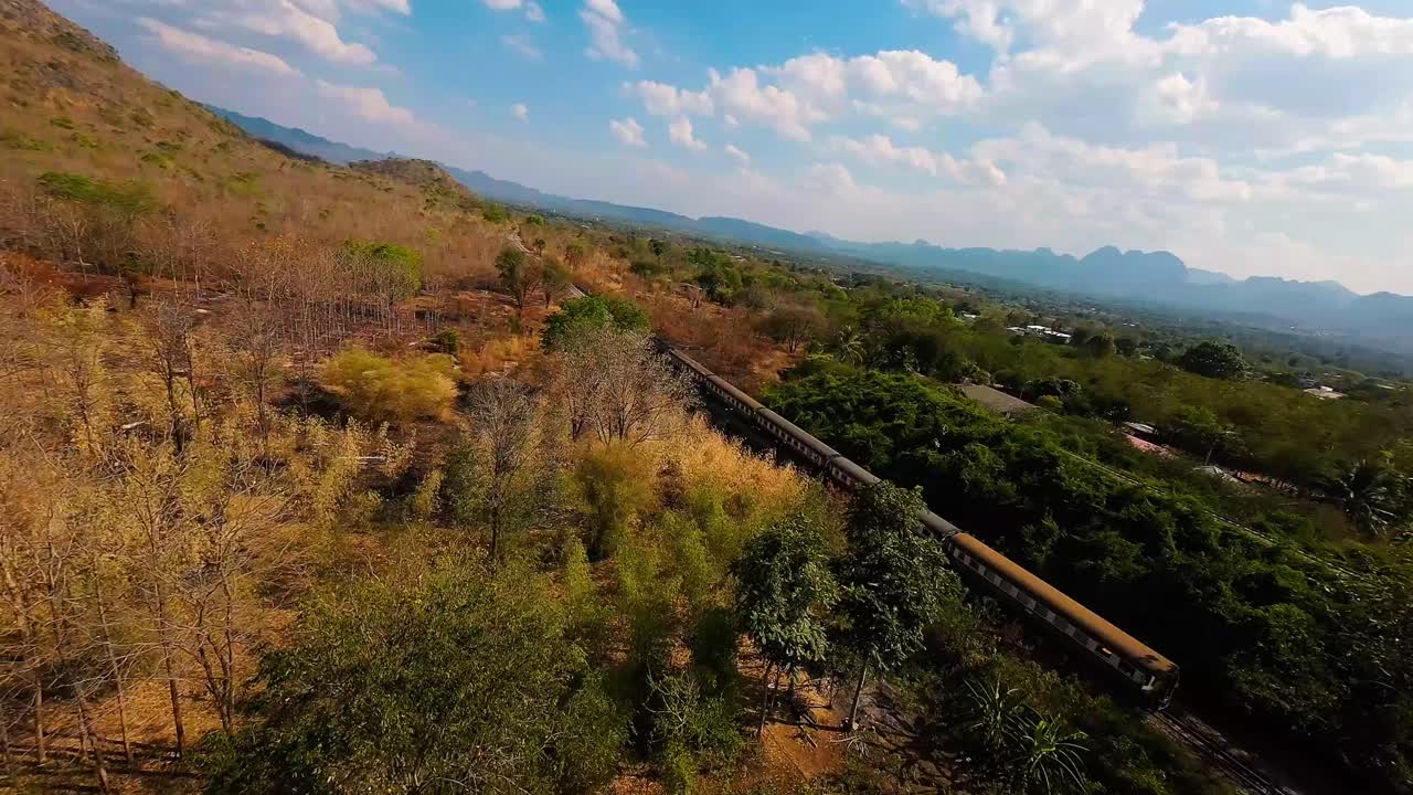 FPV drone shot approaching a train in Thailand with a forest and blue skies all around