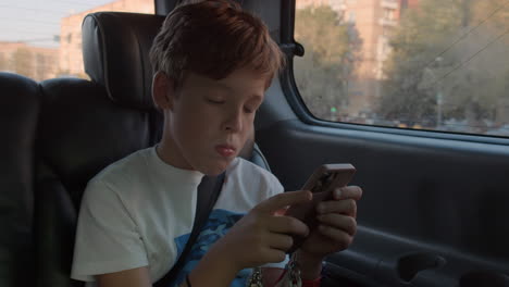 Niño-Llenando-El-Tiempo-Con-El-Teléfono-Durante-El-Viaje-En-Auto