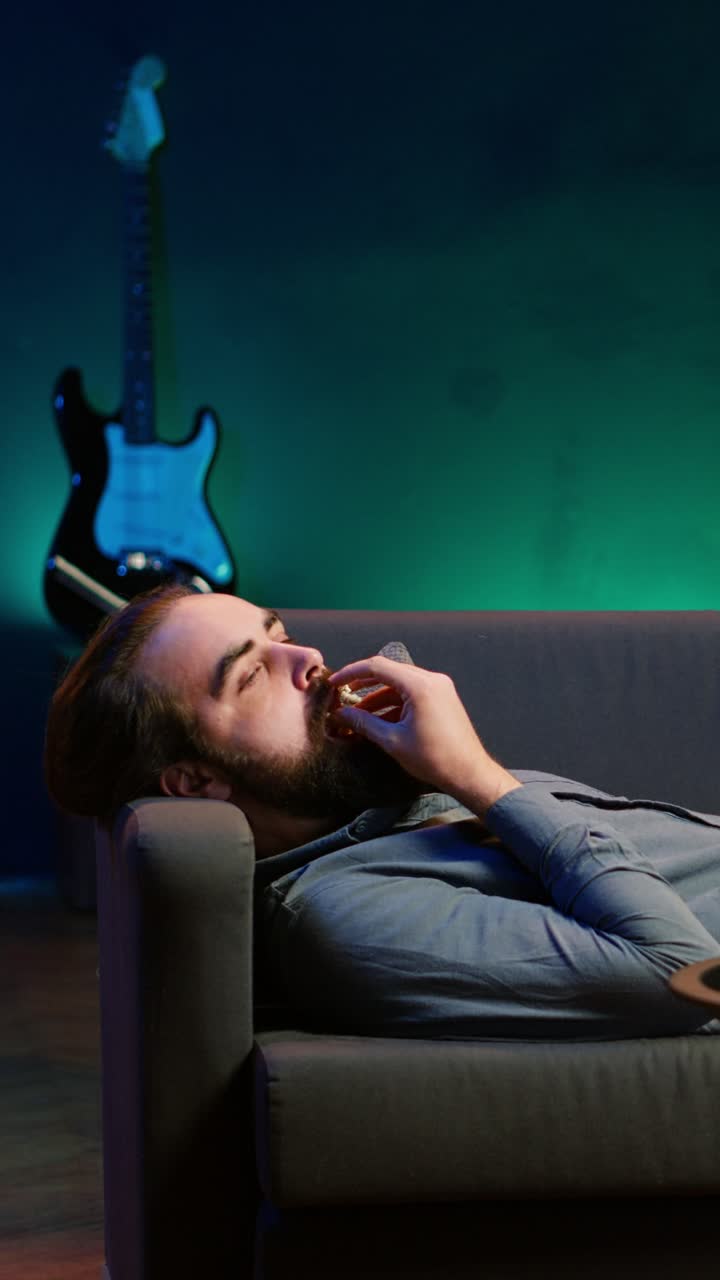 Vertical video Smiling man lounged on couch at home eating popcorn, watching TV