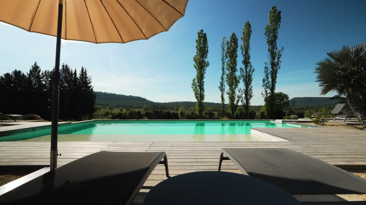 Slow rising shot over sun loungers and umbrella beside a private villa pool