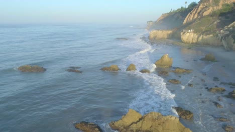 Aerial-shots-of-El-Matador-beach-over-breaking-waves-and-rocks-on-a-hazy-summer-morning-in-Malibu,-California