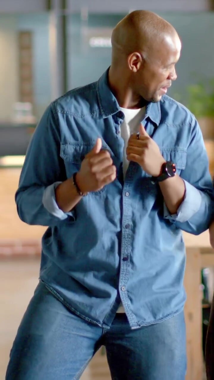 Vertical video: Noticing friend at right, adult man dancing while gripping denim collar in cafe