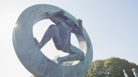 panning shot to sun poking out behind the vigeland sculpture, man in the circle