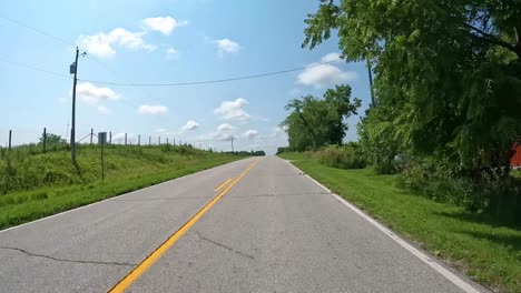 pov - slowly driving on a rural road past a farm yard and fields with fences in central iowa in late summer